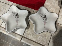 two white dishes with designs on them sitting on a tile floor next to a red towel