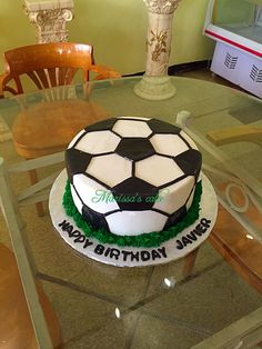 a soccer themed birthday cake sitting on top of a glass table with chairs and vases