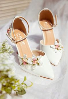 two white shoes with flowers on them sitting on a table next to a flower bouquet