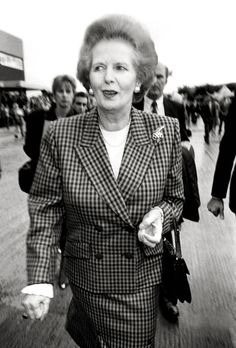 an older woman in a suit walking down the street with other people on either side