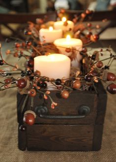 some candles are sitting in a wooden box with berries and berries around it on the table