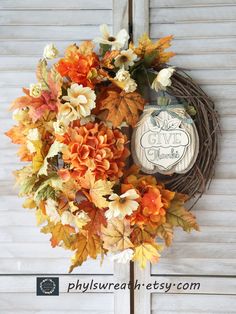 an autumn wreath hanging on the side of a door with leaves and flowers around it