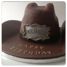 a birthday cake with a cowboy hat and name written on the front, sitting on top of a table