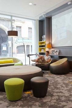 a man is sitting in a living room with chairs and ottomans on the floor next to a projector screen