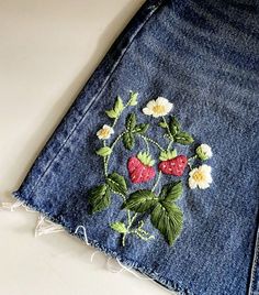 a pair of jeans with embroidered strawberries and daisies on the side, sitting on a table