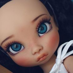 a close up of a doll with blue eyes and long black hair wearing a white dress