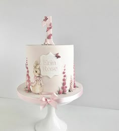 a white cake with pink frosting and bunny decorations on the top is sitting on a pedestal