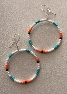 two pairs of beaded hoop earrings sitting on top of a white leather surface next to each other