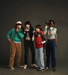 four people are taking pictures with their cell phones while standing in front of a gray background