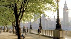 people are walking on the sidewalk in front of big ben and the houses of parliament