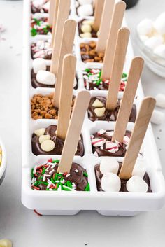 an ice tray filled with marshmallows, chocolate and pretzel pops