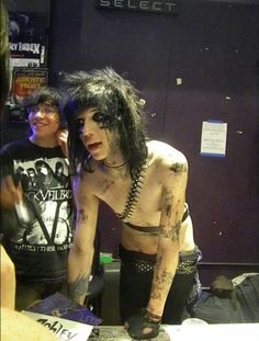 a man with tattoos and piercings standing in front of another man who is talking on the phone