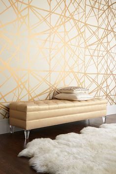 a couch sitting on top of a wooden floor in front of a wall with gold lines