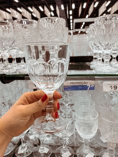 a woman holding up a wine glass in front of other glasses on display at a store