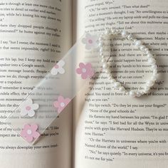 an open book with pink and white paper flowers on it next to a pearl bracelet