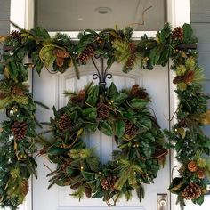 a wreath with pine cones and evergreen leaves hanging on the front door to welcome guests