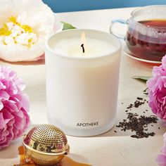 a white candle sitting on top of a table next to pink flowers and a teapot