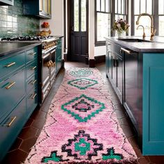 a pink and green rug in a kitchen next to blue cupboards with gold handles