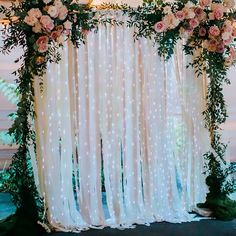 the wedding arch is decorated with white and pink flowers, greenery and sheer curtains