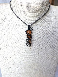 a necklace on a mannequin with an orange and black pendant