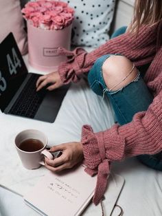 a person sitting on a bed with a laptop and cup of coffee in front of them