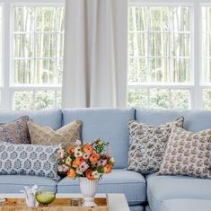 a living room with blue couches and pillows on the coffee table in front of two windows