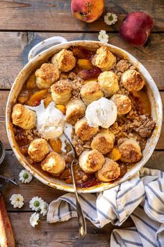 a bowl filled with fruit and ice cream on top of a wooden table next to two peaches