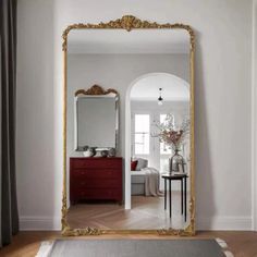 a large gold framed mirror sitting on top of a wooden floor next to a red dresser