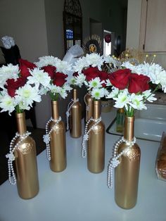 six gold vases with red and white flowers in them sitting on a counter top