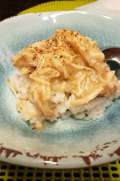 a blue plate topped with macaroni and cheese covered in gravy next to a spoon