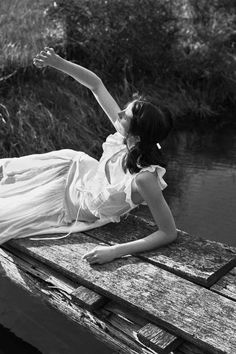 a woman laying on top of a wooden dock next to a body of water with her arms in the air