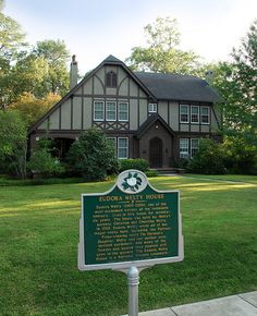 a sign in front of a large brown house with white trim on it's side