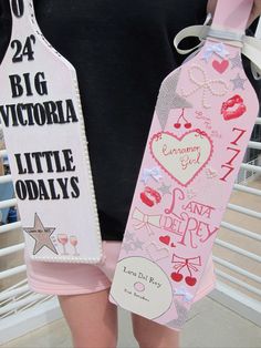 a woman holding two pink bottle shaped like tags with the words victoria and little odalys written on them