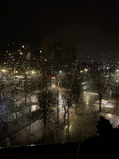 a person looking out a window at the city lights in the rain and streetlights