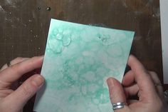 two hands holding a piece of paper with water droplets on it