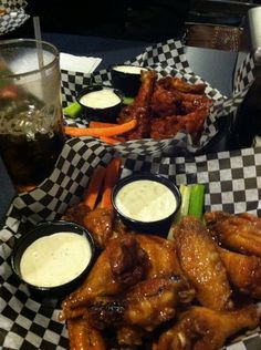 two baskets filled with wings and dips on top of a checkered table cloth