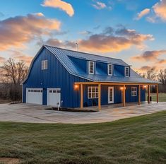 a large blue barn with two garages and lights on the side of it at sunset