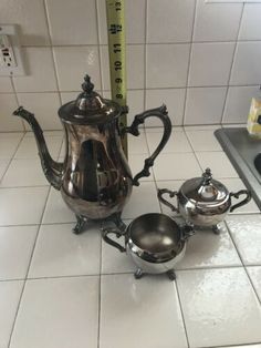 two silver teapots and a measuring tape on the floor