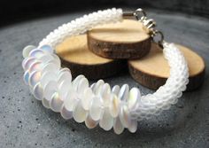 a white bracelet with glass beads and wooden discs on it's end, sitting on top of a piece of wood