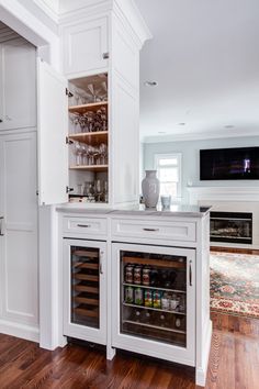 a wine cooler in the middle of a kitchen with white cabinets and wood flooring