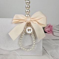 a close up of a necklace on a white box with pearls and a pink flower