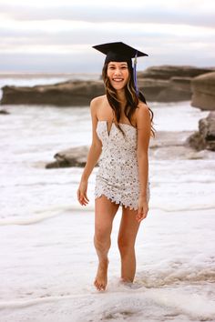 a young woman wearing a graduation cap standing in the water at the edge of the ocean