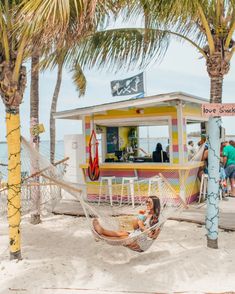 a woman laying in a hammock under a palm tree next to the beach