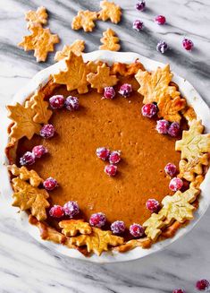 a pie with leaves and cranberries in it on a white plate next to some cookies