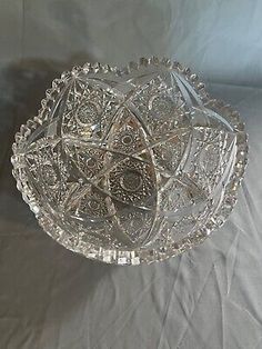 a clear glass bowl sitting on top of a white cloth covered tablecloth with an intricate design