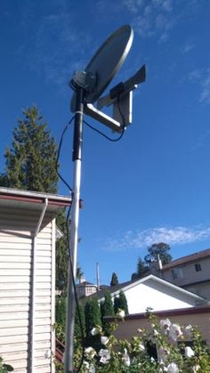 a satellite dish on top of a metal pole in front of a house with white flowers