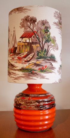 an orange lamp on a wooden table with a white and red lampshade over it