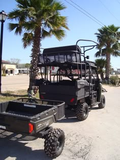 two utility vehicles parked next to each other on the side of the road near palm trees