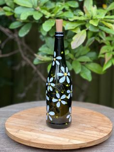 a bottle with flowers painted on it sitting on top of a wooden table next to a bush