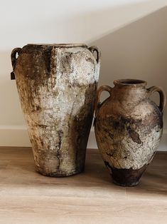 two old vases sitting on the floor in front of a white wall and wooden floor